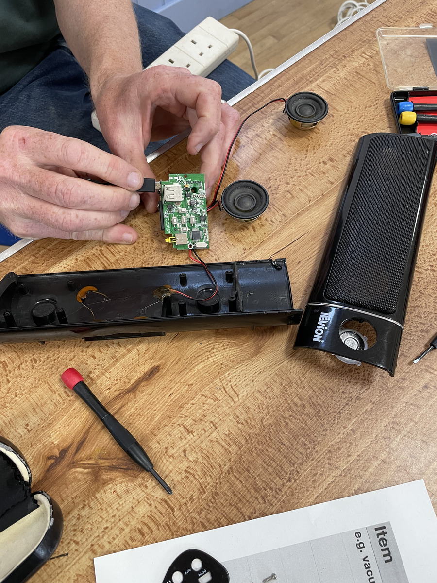 Volunteer hands repairing a small electronic circuit board on a table at Tregony Repair Café