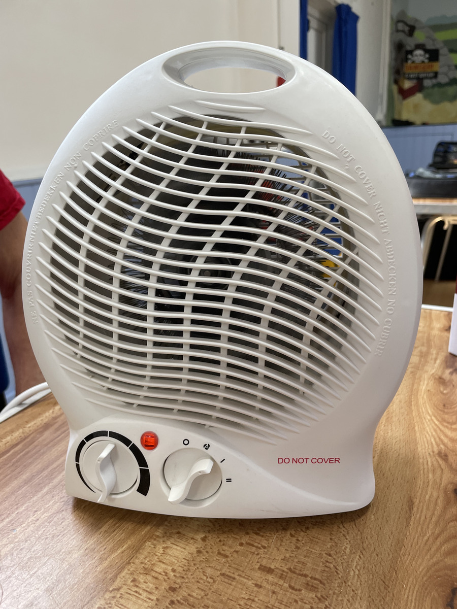 A white portable fan heater on a table awaiting repair or testing