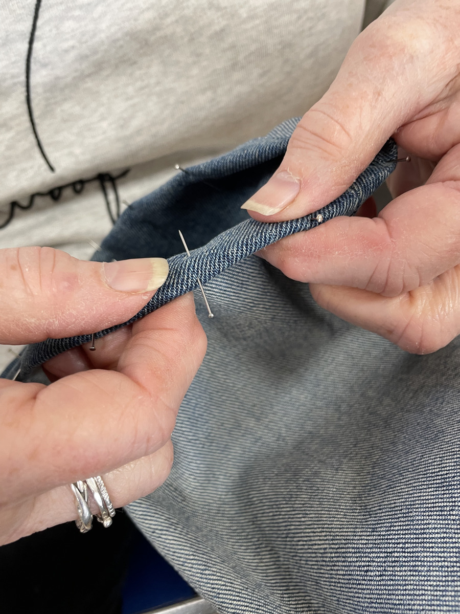 Hands sewing a small repair in blue-grey fabric at the Repair Café