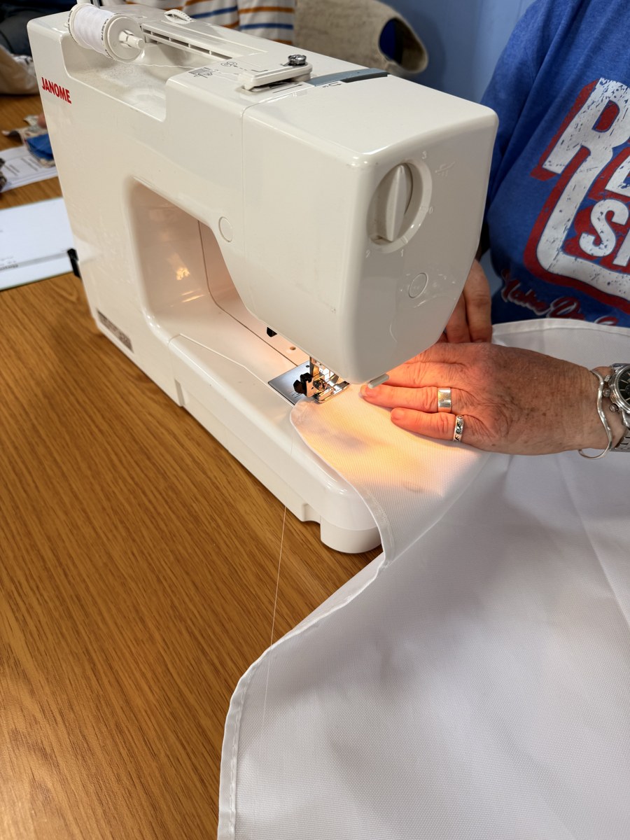 Hands guiding white fabric beneath a sewing machine’s illuminated needle area